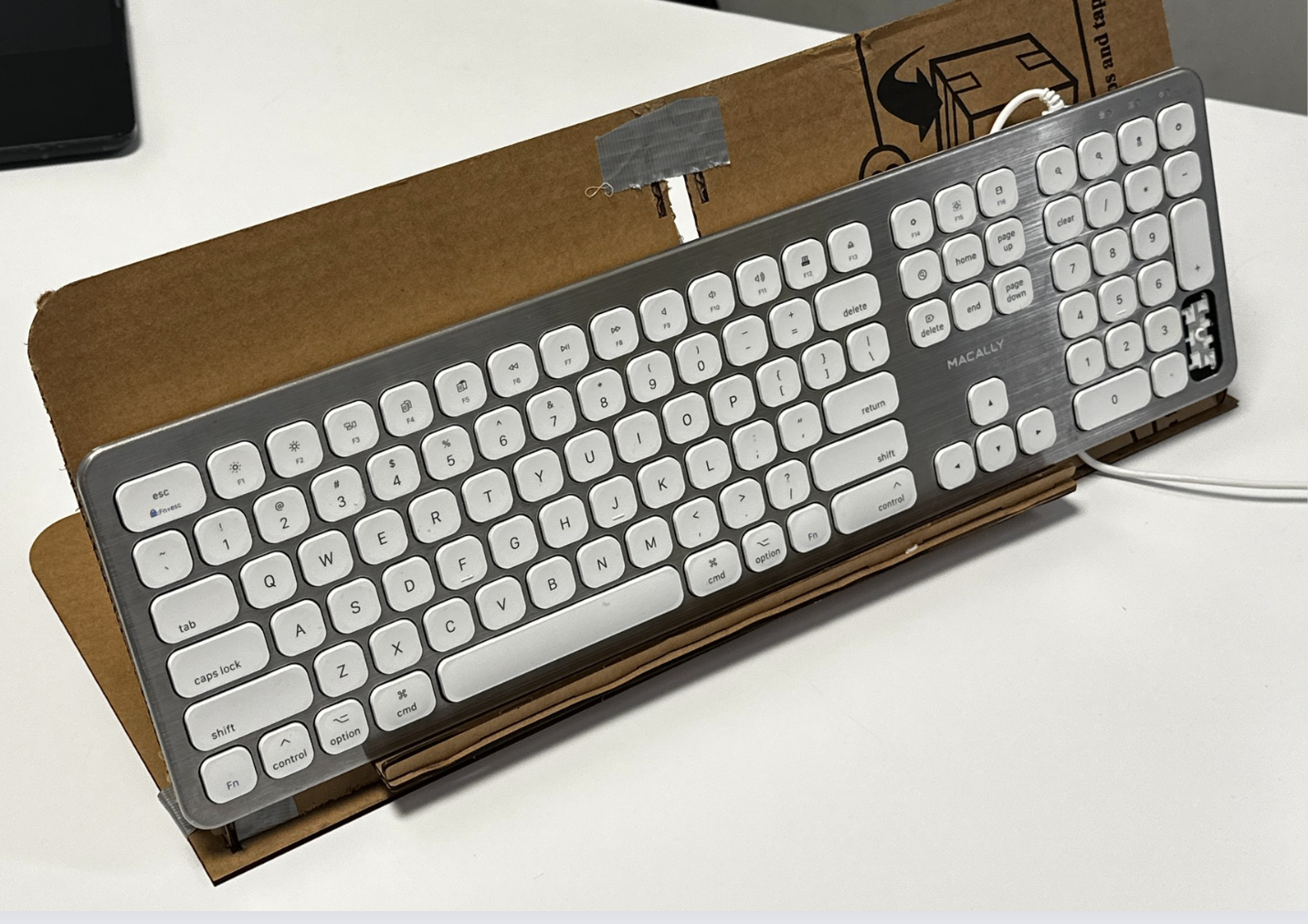A keyboard tilted on a cardboard stand prototype, built and taped by hand to test angle and heel support.